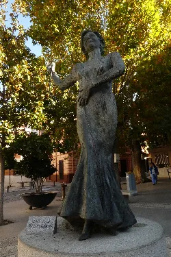 Skulptur einer Frau in langem Kleid in einem Park mit Bäumen.