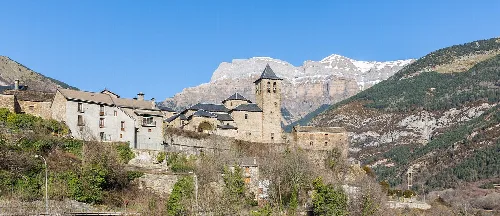 Stadt Torla mit Kirche und alten Häusern, Berge im Hintergrund.