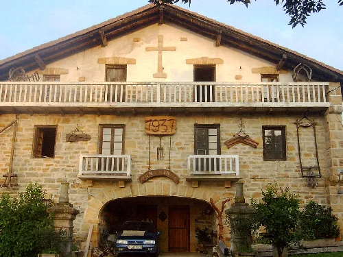 Edificio de piedra con balcones de madera y cruz en la parte superior.