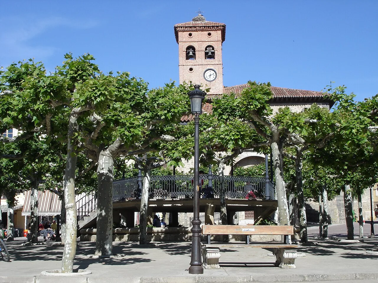 Hauptplatz mit Bäumen, Bank und Uhrturm in Belorado.