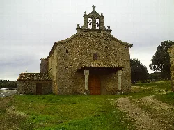 Small stone church with bell tower and wooden door in a rural setting.