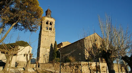 Iglesia parroquial de Alcocer con torre y árboles alrededor.