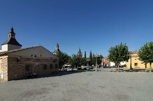 Square with trees, historic buildings, and a church in Ugena.