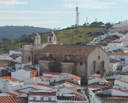 Our Lady of the Assumption church in Segura de León, with white houses and green hills.