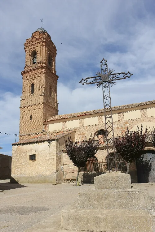 Kirchturm und ein schmiedeeisernes Kreuz im Vordergrund.