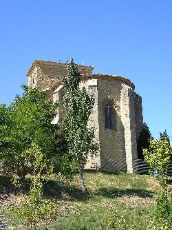 Stone church with narrow windows and green trees in the foreground.