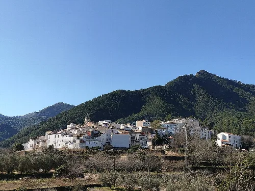 Pueblo de Ahín con casas blancas en una ladera y montañas verdes al fondo.