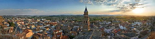 Panorámica de Arguedas con iglesia y casas tradicionales al atardecer.