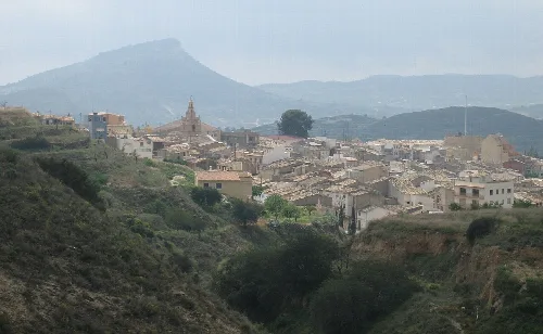 Vista de un pueblo en una ladera con montañas al fondo.