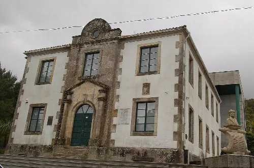 Edificio de la casa consistorial de Carnota con fachada de piedra y escultura en el lateral.