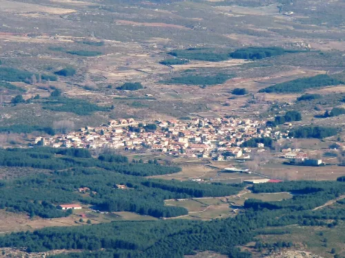 Luftaufnahme eines Dorfes in einem Tal, umgeben von Feldern und Bergen.