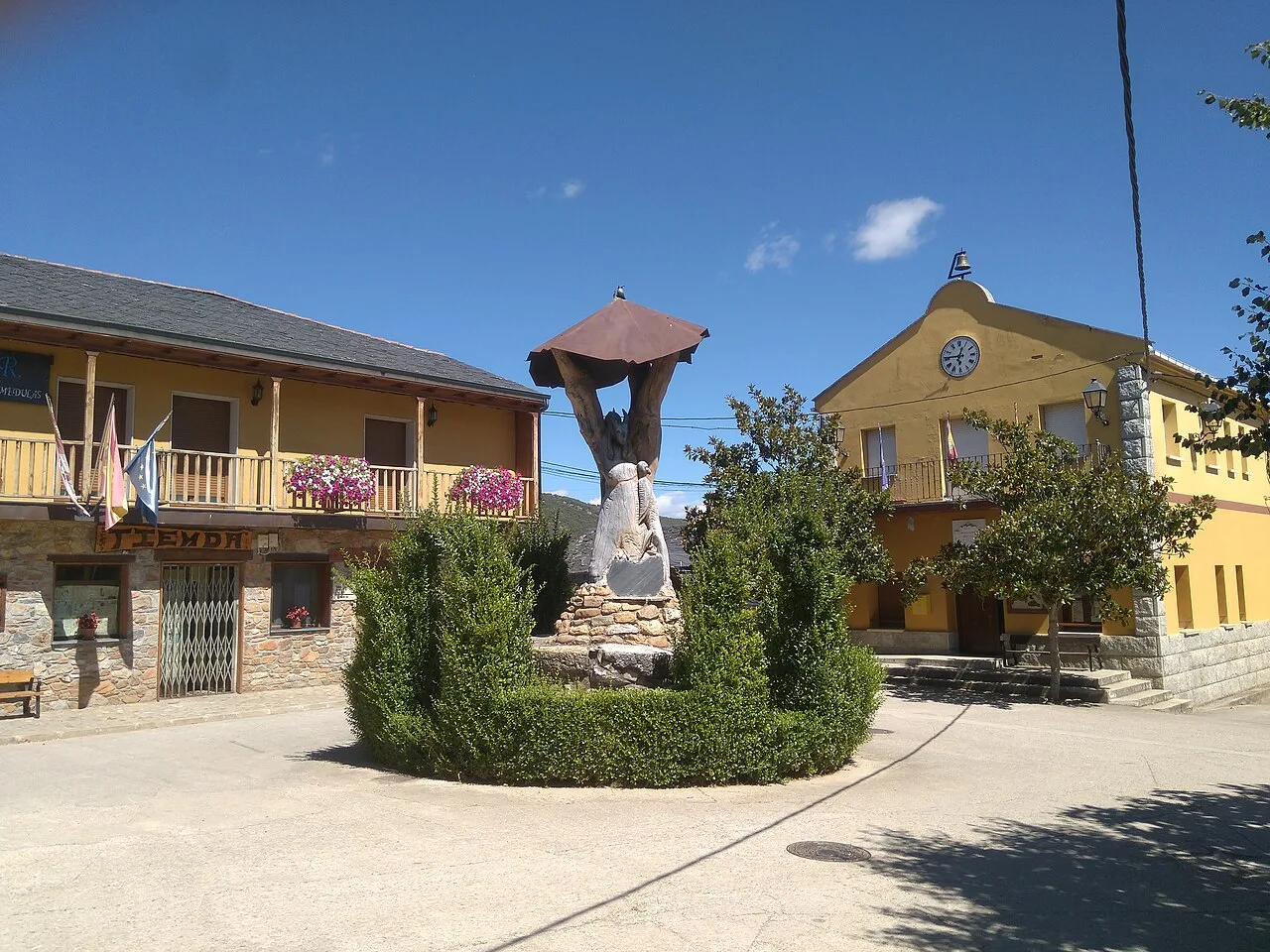 En esta fotografía aparece la plaza principal de Borrenes, en cuyo centro aparece una escultura de madera, que recrea una antigua picota o lugar de ajusticiamiento. En el frente se sitúa la fachada principal del Ayuntamiento.