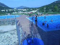 Personas en la piscina de Benigembla con vistas al pueblo y montañas.