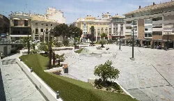 Square with palm trees, benches, and buildings in the background.