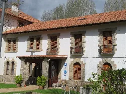 Edificio de balneario con fachada blanca, ventanas con persianas de madera y un pequeño jardín.