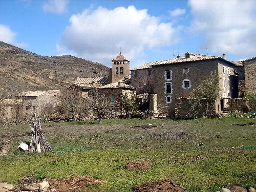 Vista de casas antiguas y una iglesia en Longás con montañas al fondo.