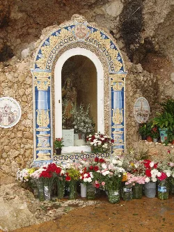 A shrine with a statue of the Virgin of Carmen in a decorated niche with flowers and tiles.