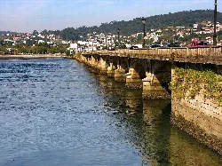 Stone bridge over the Eume River in Cabanas, with cars and urban landscape.