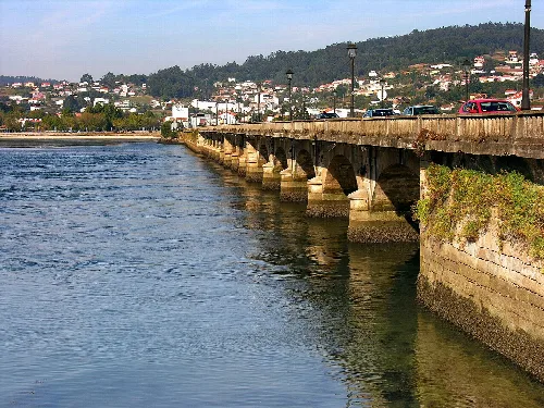 Stone bridge over the Eume River in Cabanas, with cars and urban landscape.
