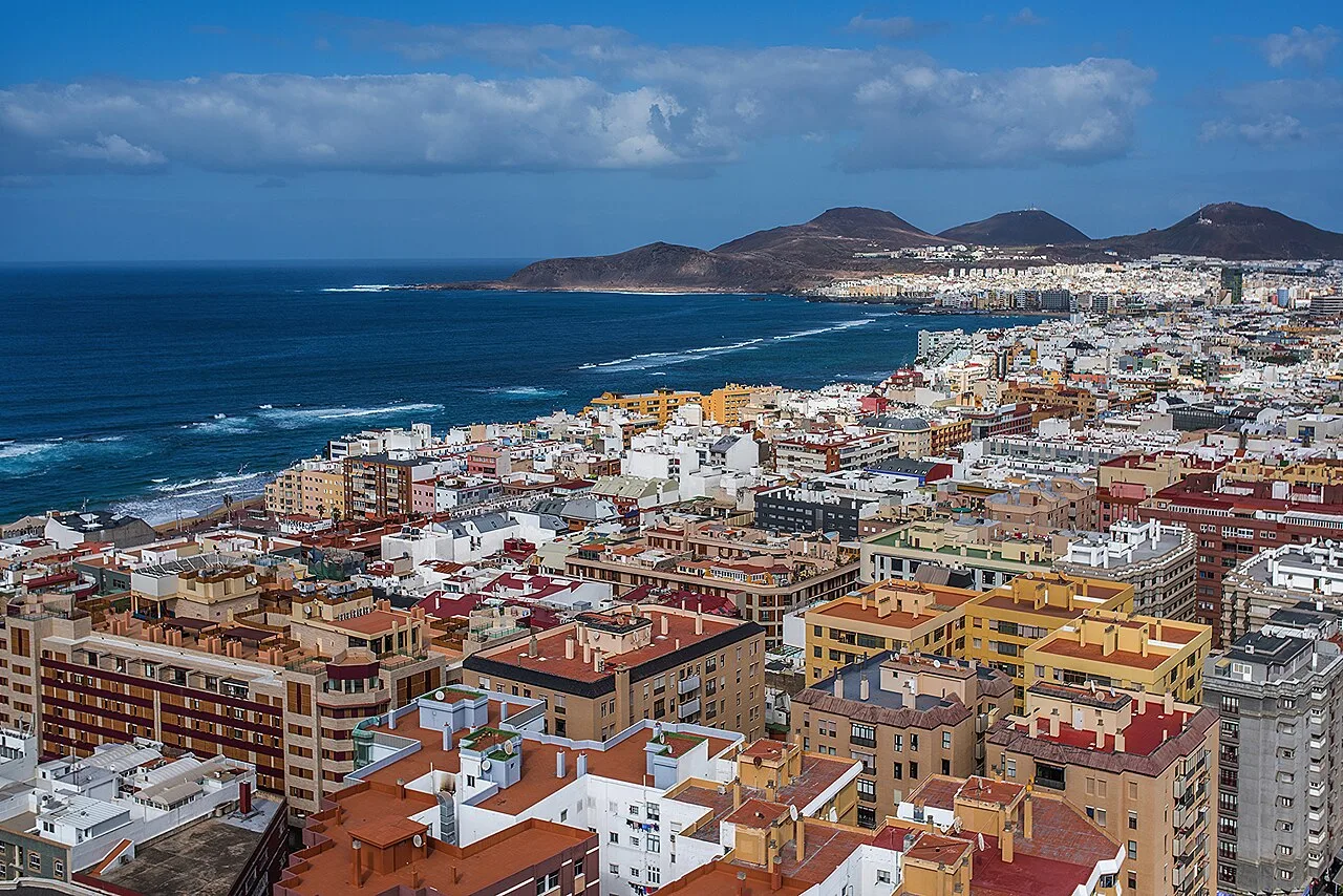 Luftaufnahme von Gebäuden in Las Palmas mit Meer und Bergen im Hintergrund.