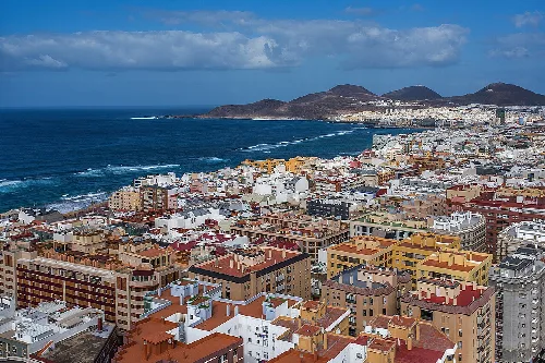 Luftaufnahme von Gebäuden in Las Palmas mit Meer und Bergen im Hintergrund.