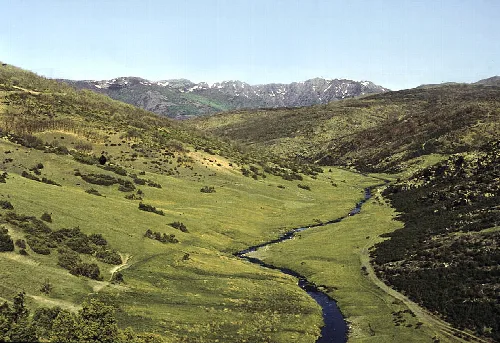 Valles verdes con río y montañas en el fondo.