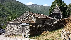 Steinhaus mit Ziegeldach und Bergen im Hintergrund.