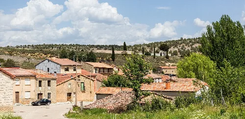 Steinhäuser mit Ziegeldächern in Muriel de la Fuente, Soria, unter einem blauen Himmel mit Wolken.