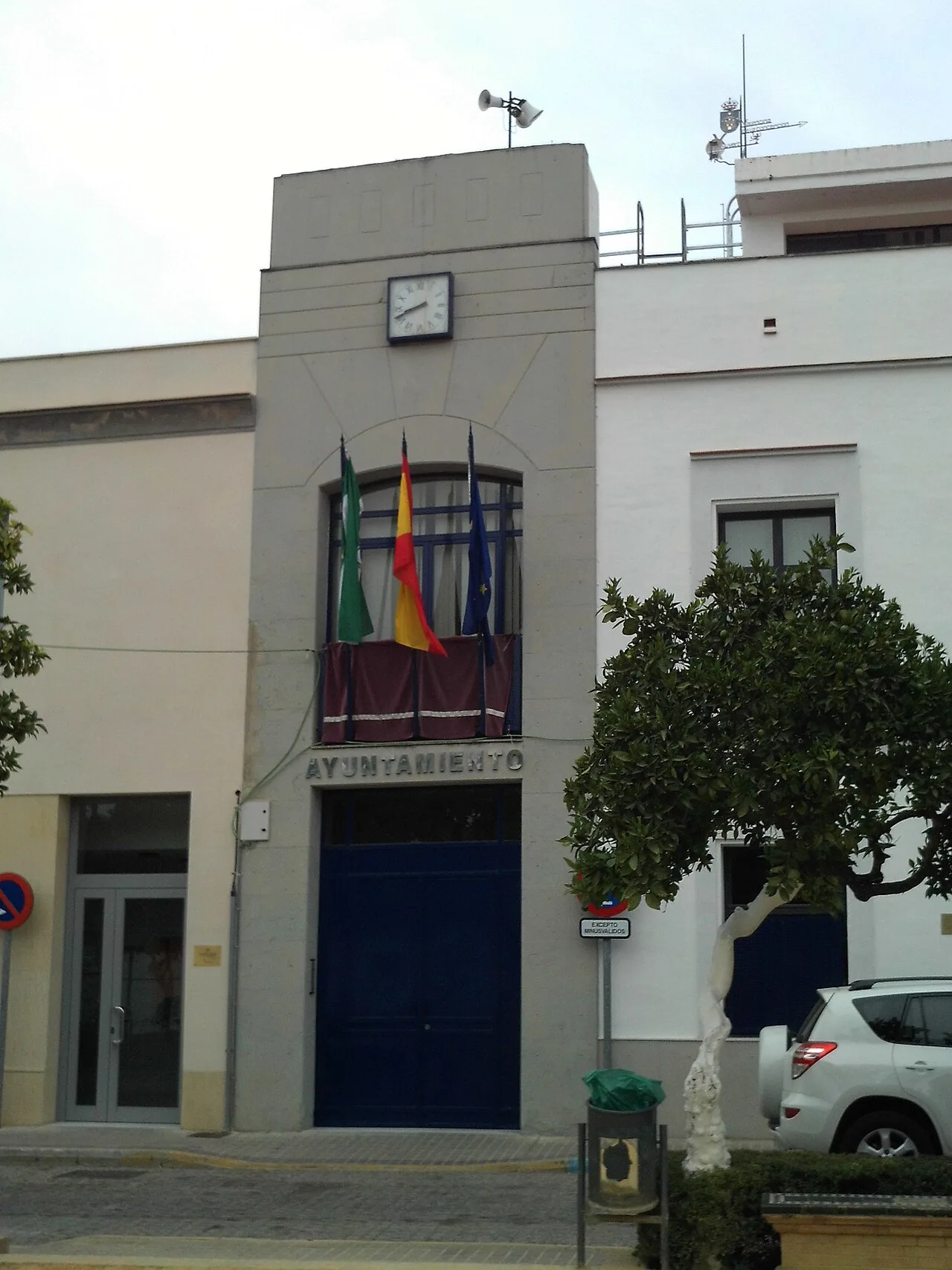 Edificio del ayuntamiento con banderas y reloj en la fachada.