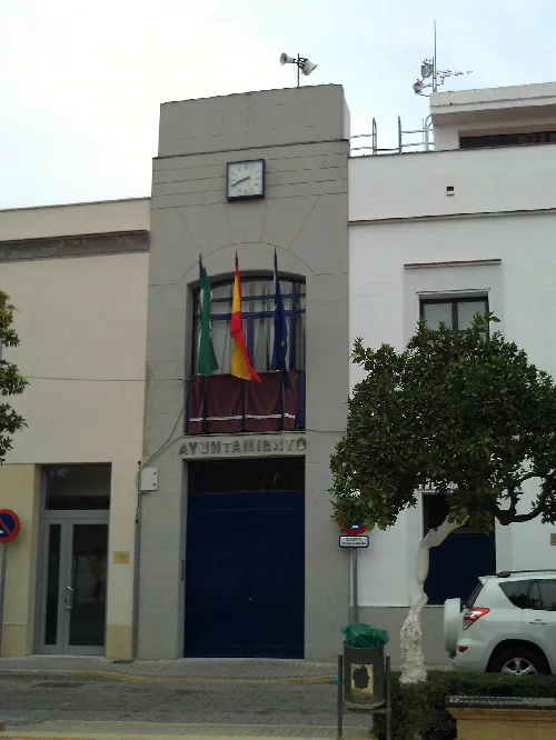 Edificio del ayuntamiento con banderas y reloj en la fachada.