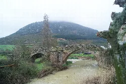 Ancient stone bridge over a river in Monreal, Navarra, with a foggy mountain.