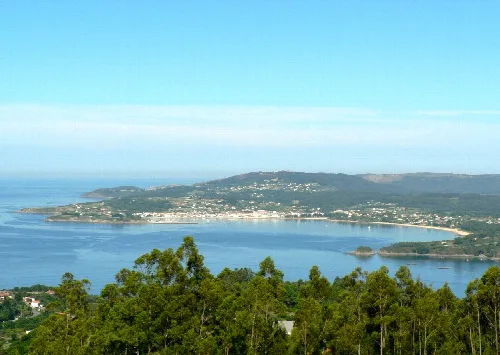 Vista de la ría de Ares con vegetación y pueblo en el horizonte.
