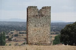Torreón de piedra en un campo con árboles y colinas al fondo.
