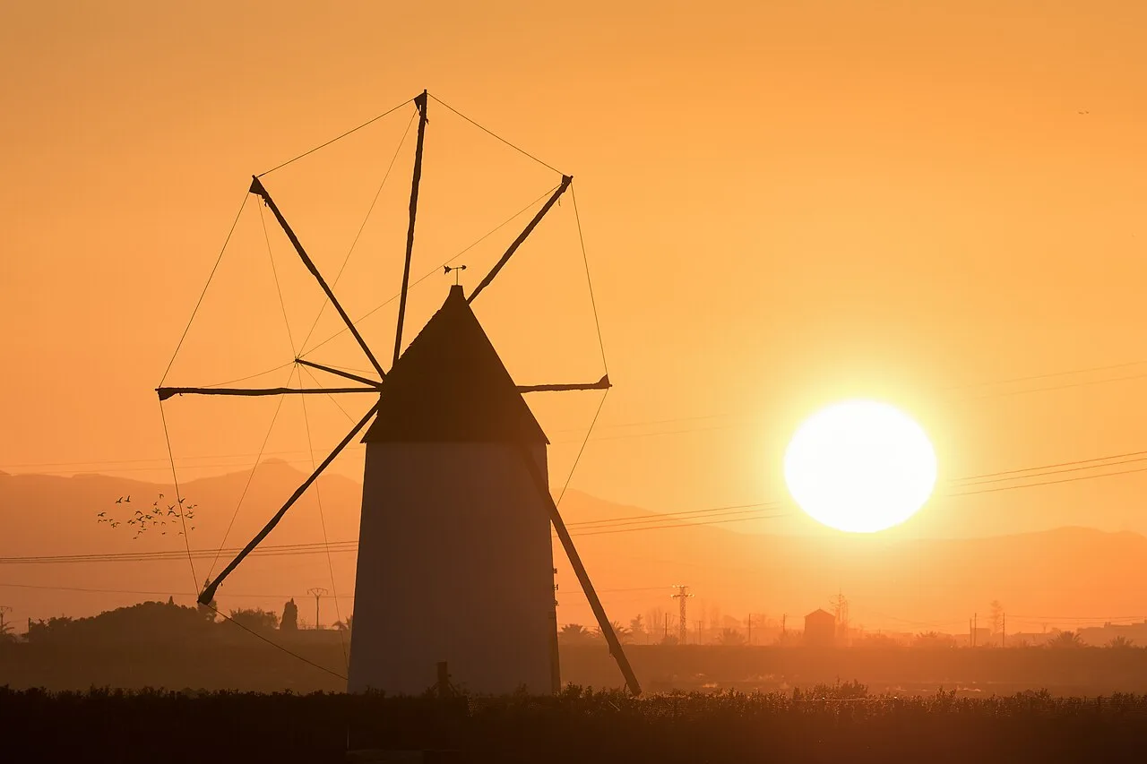 Molino de viento en un campo con el sol poniente.