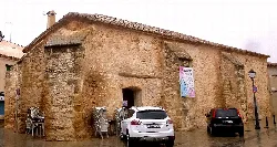 Stone building in Mota del Cuervo with a sign and parked cars on the street.