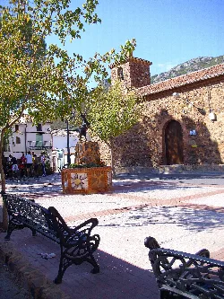 Square with benches, trees, and a stone church in Solana del Pino.