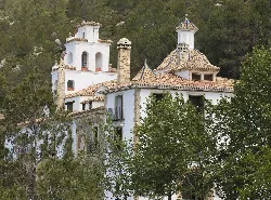 White church with towers and domes surrounded by trees and hills.