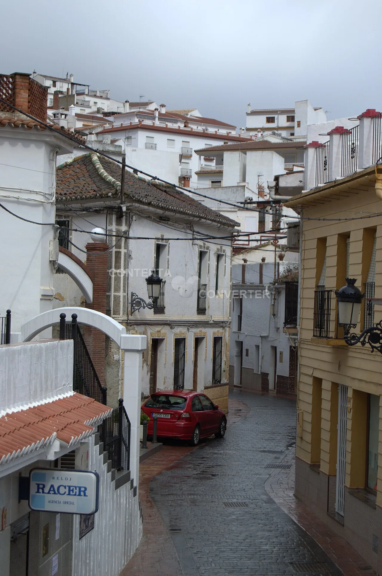 Narrow street with white houses and a red car in Periana, Málaga.