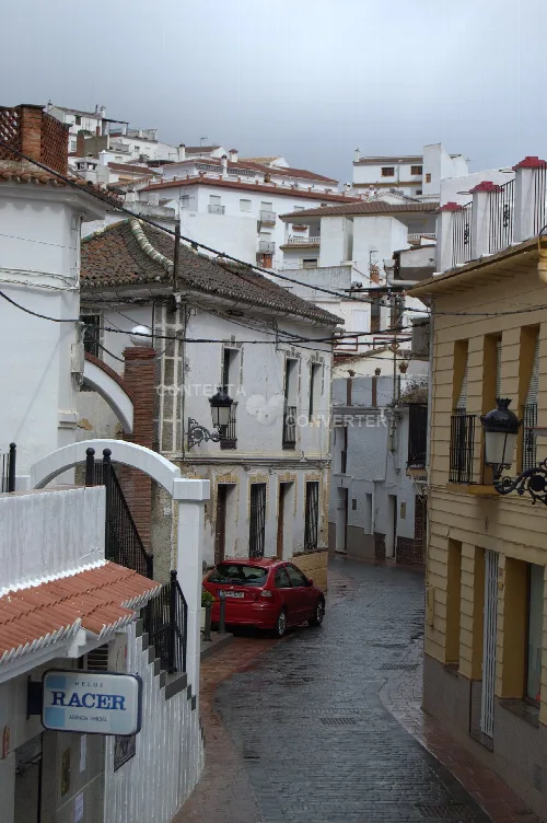 Enge Straße mit weißen Häusern und rotem Auto in Periana, Málaga.