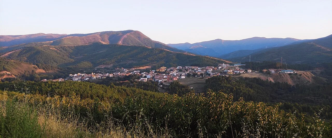 Landschaft mit Stadt umgeben von Bergen und Vegetation.