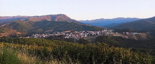 Landschaft mit Stadt umgeben von Bergen und Vegetation.