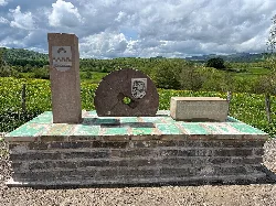 Monumento en Burguete con inscripciones y escudos, en un paisaje rural.