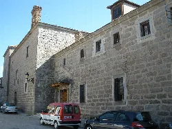 Stone facade of a monastery with small windows and parked cars.