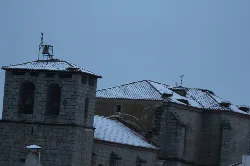 Iglesia de piedra con campanario y nieve en los tejados en Alaraz