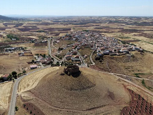 Vista aérea de un castillo en una colina y un pueblo en un paisaje rural.