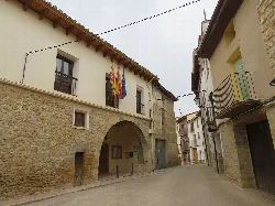 Straße in Las Parras de Castellote mit Steingebäuden und Flaggen.