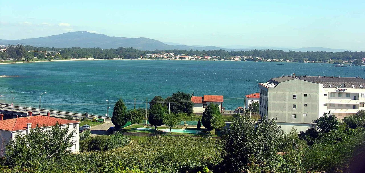Landschaft der Ría de Arousa mit blauem Wasser und nahegelegenen Gebäuden.