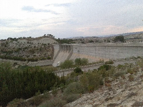 Große Staumauer in einer trockenen Landschaft mit Vegetation und Hügeln.