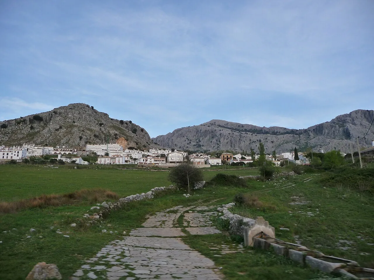 Camino de piedra en primer plano con pueblo y montañas en el fondo.