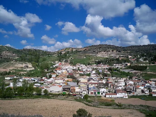 Panoramic view of Loranca de Tajuña with houses and hills under a cloudy sky.